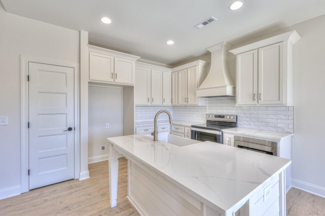 kitchen with light wood-type flooring, a sink, tasteful backsplash, stainless steel electric range oven, and custom exhaust hood