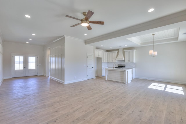 unfurnished living room with light wood-type flooring, a raised ceiling, ornamental molding, recessed lighting, and baseboards