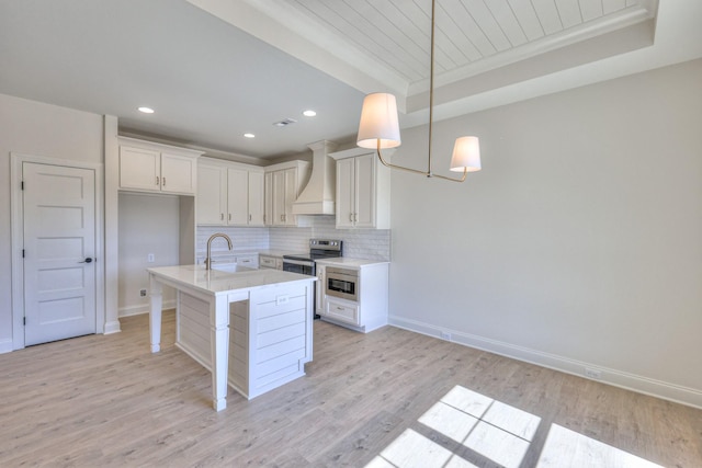 kitchen featuring light wood-style flooring, a sink, stainless steel appliances, decorative backsplash, and custom exhaust hood