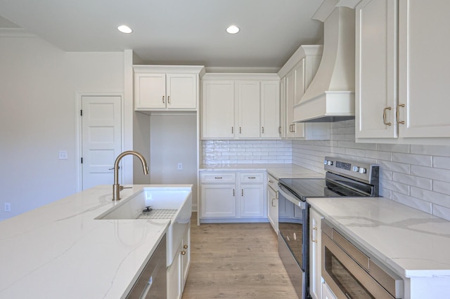 kitchen with light stone counters, custom exhaust hood, stainless steel electric range, white cabinets, and light wood-type flooring