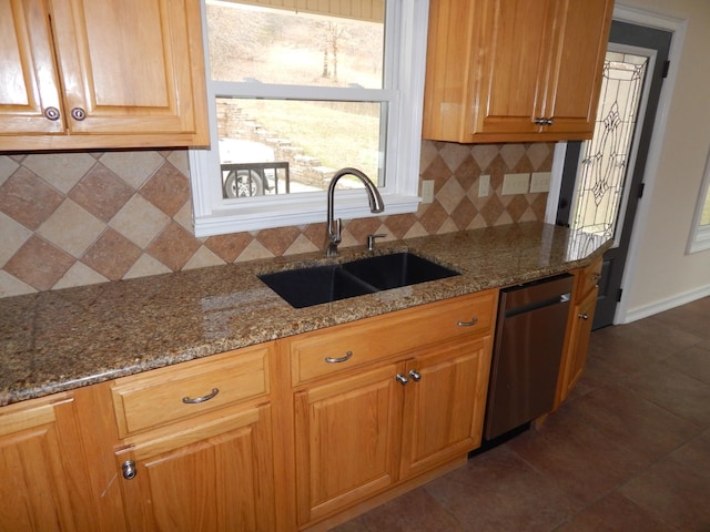 kitchen featuring stainless steel dishwasher, dark stone counters, tasteful backsplash, and a sink