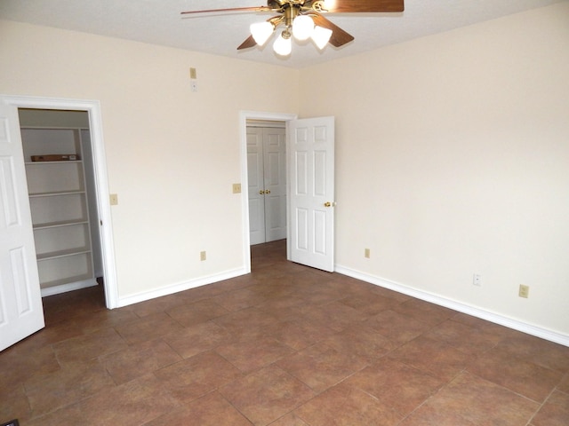 unfurnished bedroom with a closet, ceiling fan, a walk in closet, and baseboards