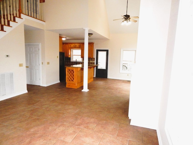 unfurnished living room featuring baseboards, visible vents, decorative columns, ceiling fan, and a towering ceiling