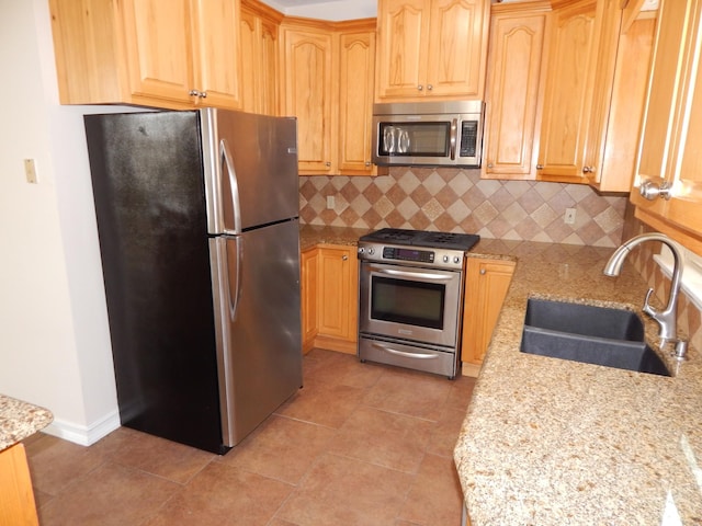 kitchen with a sink, stainless steel appliances, light stone countertops, and backsplash