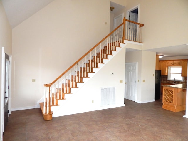 staircase featuring visible vents, a high ceiling, and baseboards