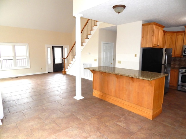 kitchen with backsplash, open floor plan, stainless steel appliances, dark stone counters, and a breakfast bar area