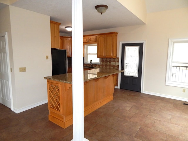 kitchen featuring a sink, freestanding refrigerator, dark stone counters, decorative backsplash, and baseboards