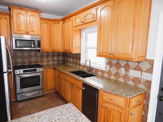 kitchen with light stone countertops, dark tile patterned flooring, a sink, appliances with stainless steel finishes, and tasteful backsplash