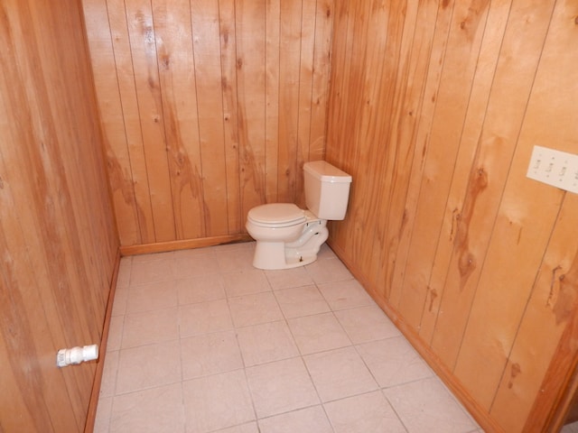 half bath featuring tile patterned floors, wood walls, and toilet