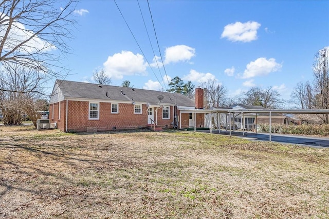 back of house featuring a chimney, driveway, crawl space, an attached carport, and brick siding