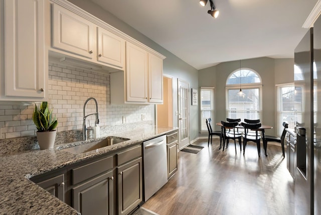 kitchen featuring a sink, wood finished floors, light stone countertops, dishwasher, and vaulted ceiling