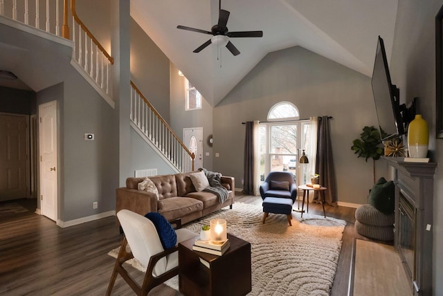 living area featuring baseboards, a fireplace with flush hearth, stairs, wood finished floors, and high vaulted ceiling