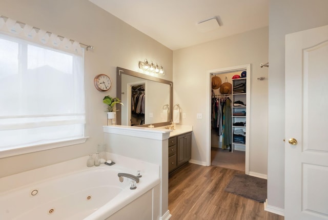 bathroom with vanity, a spacious closet, wood finished floors, and a whirlpool tub