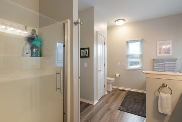 bathroom with a shower stall, toilet, baseboards, and wood finished floors