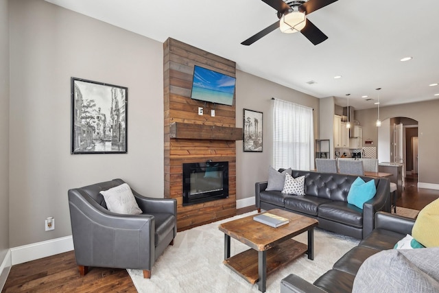 living area with a ceiling fan, a large fireplace, arched walkways, light wood-style floors, and baseboards