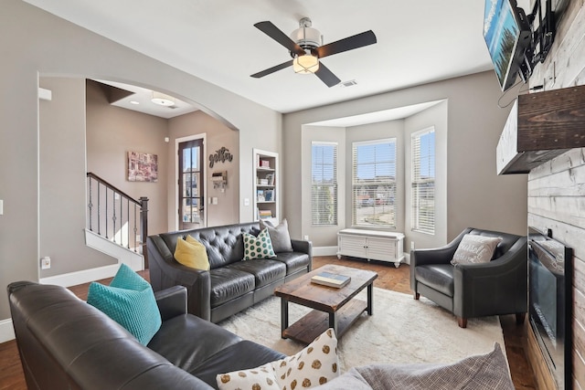 living room featuring visible vents, arched walkways, a fireplace, baseboards, and stairs