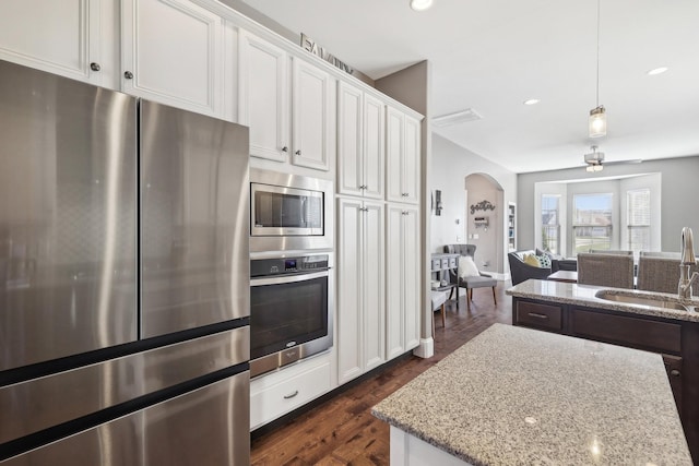 kitchen featuring a sink, light stone counters, arched walkways, appliances with stainless steel finishes, and white cabinets