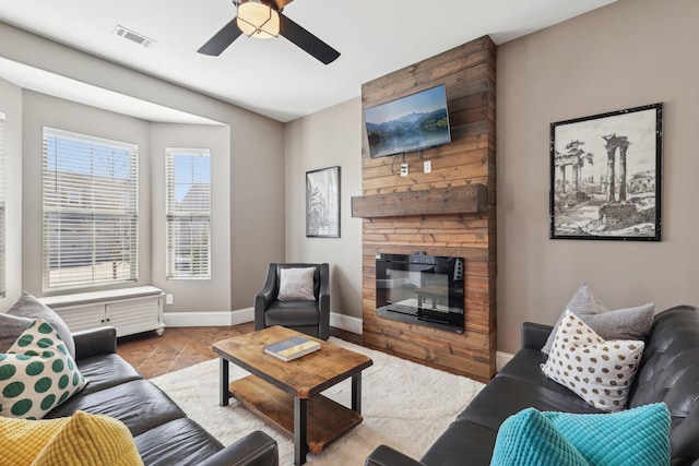 living room featuring ceiling fan, a fireplace, visible vents, and baseboards