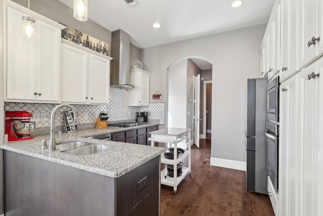 kitchen featuring a sink, dark wood-style floors, stainless steel appliances, arched walkways, and wall chimney exhaust hood