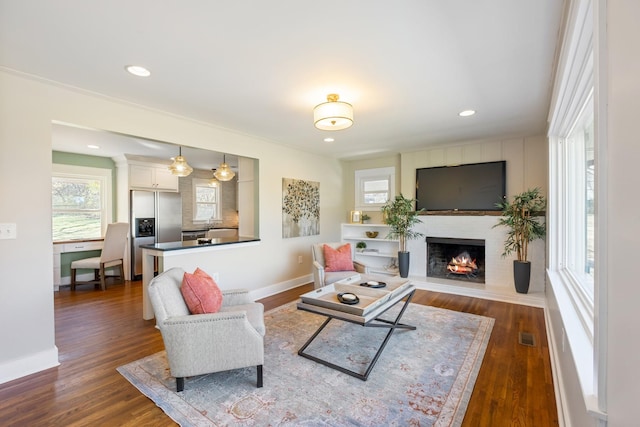 living area featuring a large fireplace, visible vents, dark wood-type flooring, and baseboards