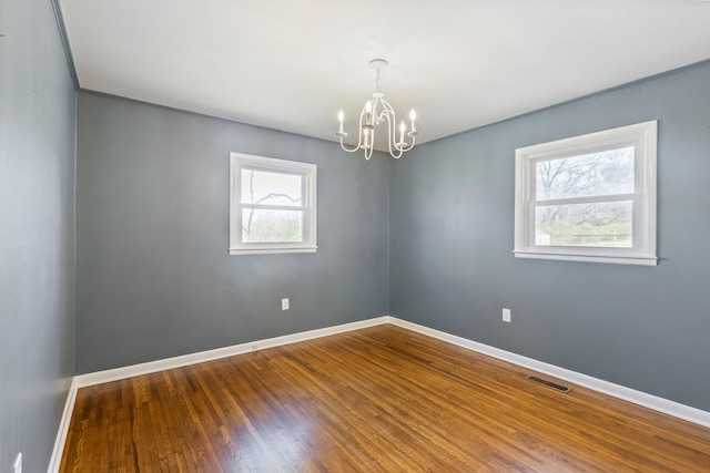 spare room with visible vents, baseboards, a notable chandelier, and wood finished floors