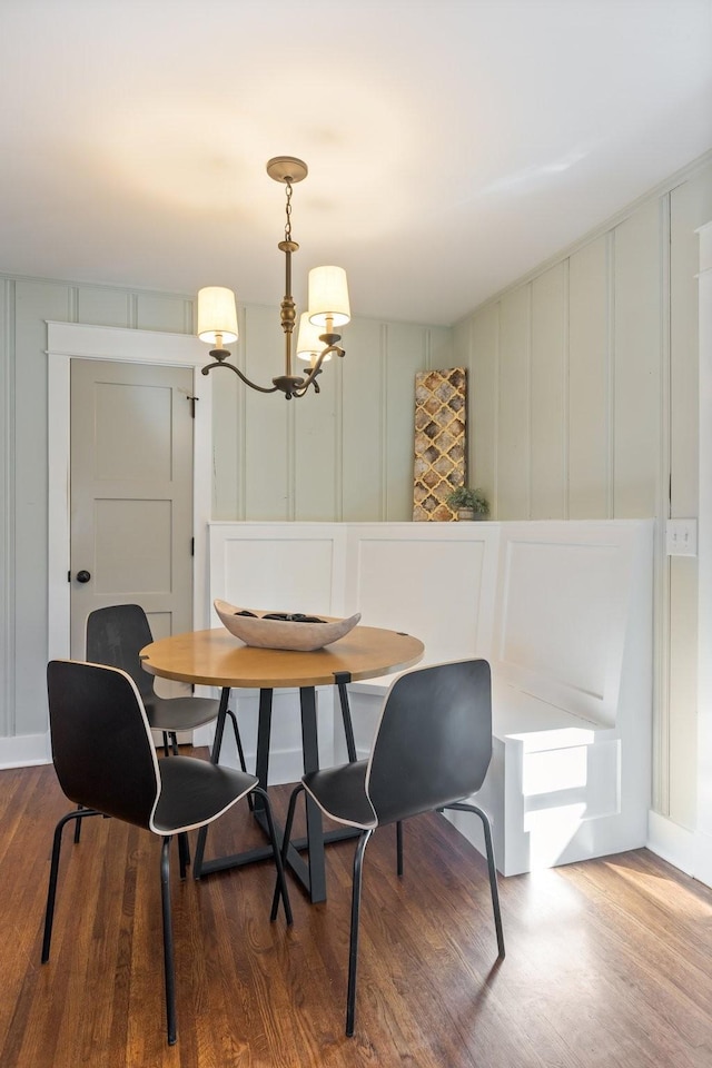 dining area with a chandelier, a decorative wall, breakfast area, and wood finished floors