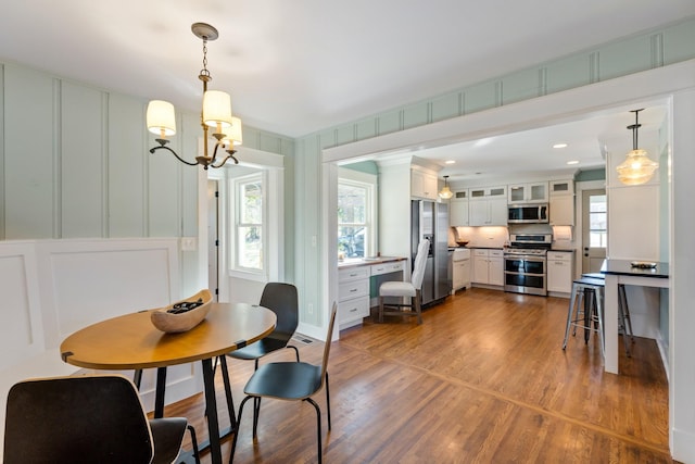 dining area with an inviting chandelier, a decorative wall, and dark wood-style floors