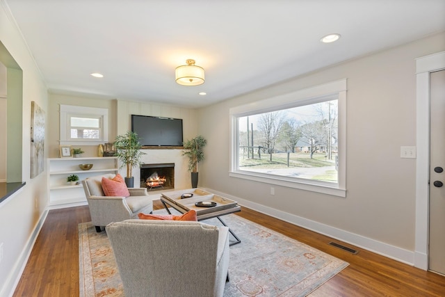 living area with wood finished floors, visible vents, a warm lit fireplace, and baseboards