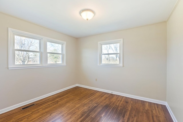 unfurnished room with dark wood finished floors, baseboards, visible vents, and a wealth of natural light