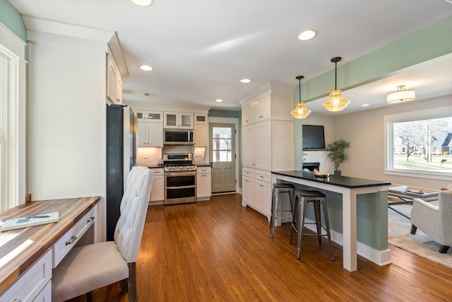 kitchen featuring dark wood-style floors, a breakfast bar, stainless steel appliances, white cabinets, and dark countertops