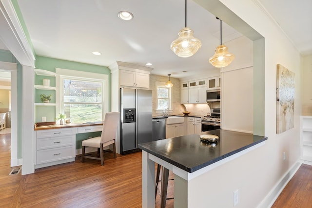 kitchen with dark wood finished floors, stainless steel appliances, a peninsula, white cabinets, and built in study area