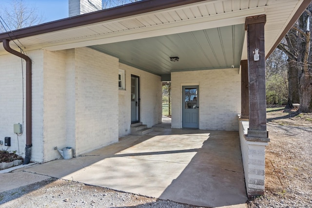 entrance to property with brick siding, driveway, a chimney, and a carport