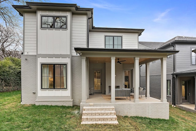 back of property with a yard, board and batten siding, brick siding, ceiling fan, and a patio area