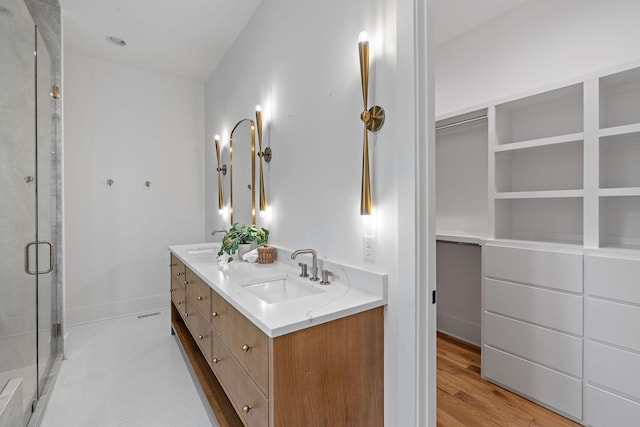 bathroom with double vanity, wood finished floors, a stall shower, and a sink