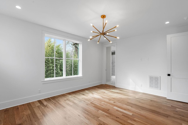 empty room with baseboards, light wood-style floors, visible vents, and a chandelier