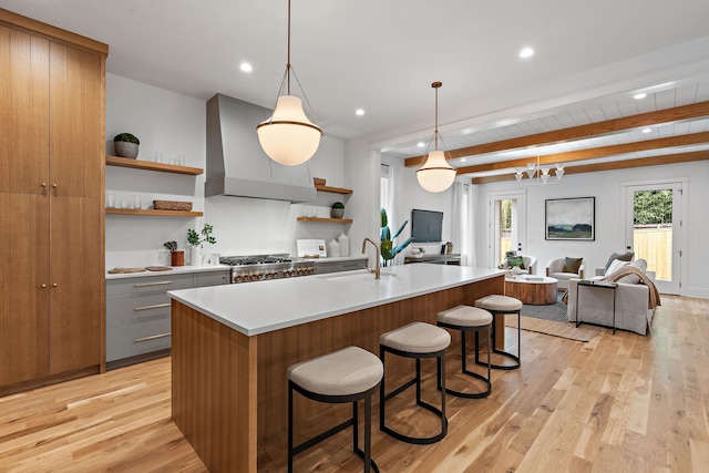 kitchen with open shelves, open floor plan, light countertops, wall chimney exhaust hood, and a sink