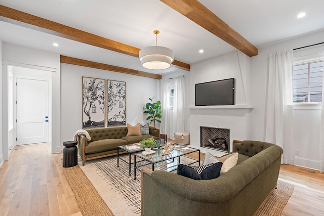 living area featuring light wood finished floors, a fireplace with flush hearth, recessed lighting, and beam ceiling