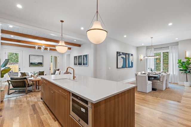 kitchen featuring light wood finished floors, a kitchen island with sink, a sink, open floor plan, and light countertops