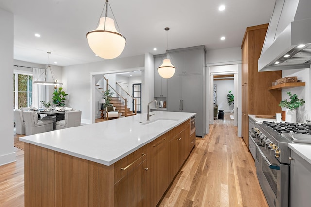 kitchen featuring a sink, double oven range, a spacious island, brown cabinetry, and wall chimney range hood