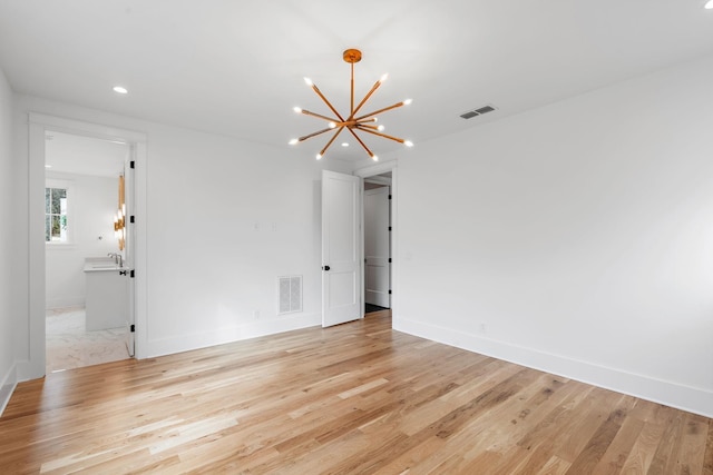 unfurnished room featuring light wood finished floors, visible vents, and a chandelier