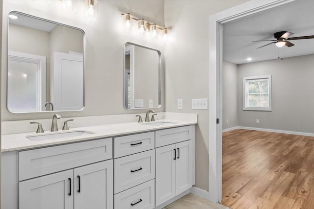 bathroom featuring wood finished floors, baseboards, double vanity, and ceiling fan