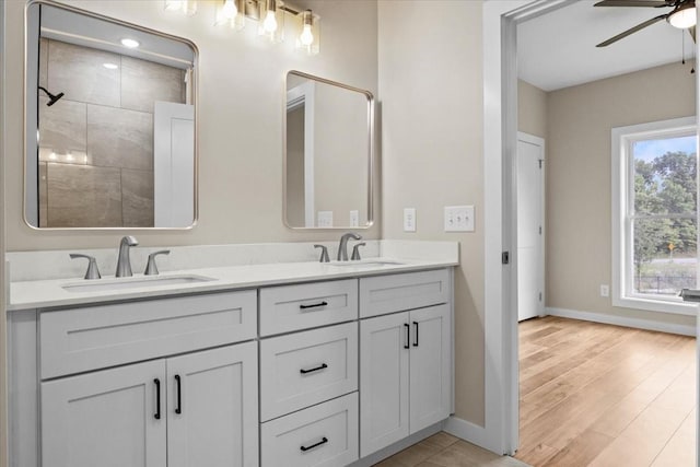full bath featuring baseboards, ceiling fan, double vanity, and wood finished floors