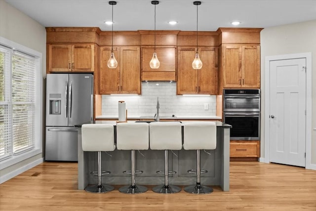 kitchen with appliances with stainless steel finishes, a sink, an island with sink, light wood-style floors, and backsplash