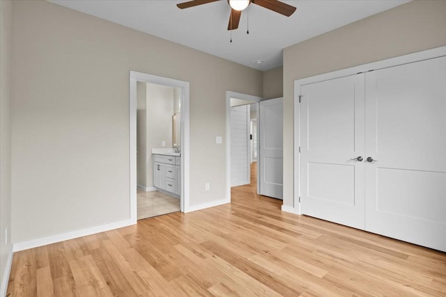 unfurnished bedroom with light wood-style floors, baseboards, a closet, a sink, and ensuite bathroom