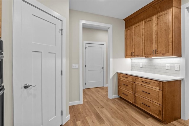 kitchen with decorative backsplash, light wood-style flooring, light countertops, baseboards, and brown cabinetry