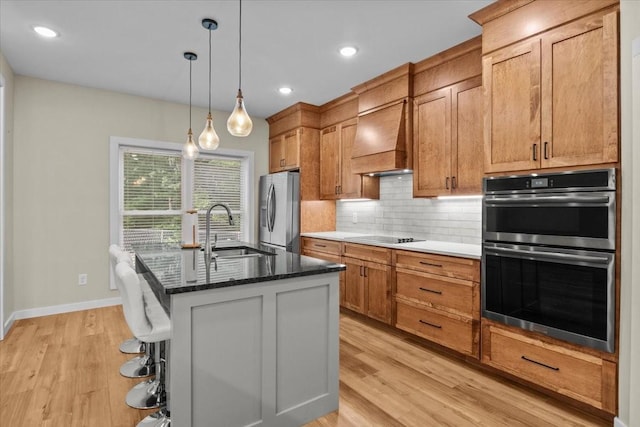kitchen with stainless steel appliances, a sink, backsplash, a kitchen island with sink, and custom range hood