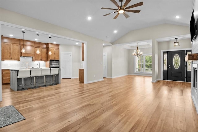 unfurnished living room with light wood-style flooring, ceiling fan, a chandelier, lofted ceiling, and a sink