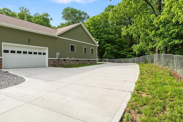 view of side of home featuring concrete driveway, fence, a garage, a shingled roof, and crawl space