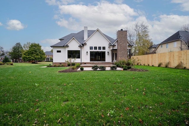 rear view of house featuring a chimney, fence, a lawn, and crawl space