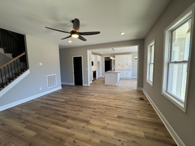 unfurnished living room featuring stairs, wood finished floors, visible vents, and baseboards